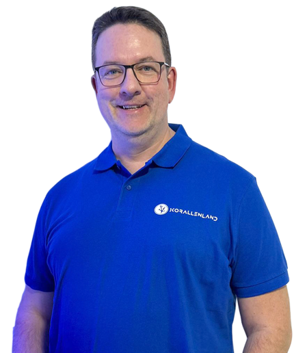 Gerd Raabe - Inhaber Korallenland Gerd Raabe in blauem Polo-Shirt lächelt, vor einem weißen Hintergrund.