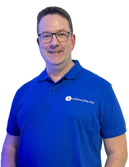 Gerd Raabe - Inhaber Korallenland Gerd Raabe in blauem Polo-Shirt lächelt, vor einem weißen Hintergrund.